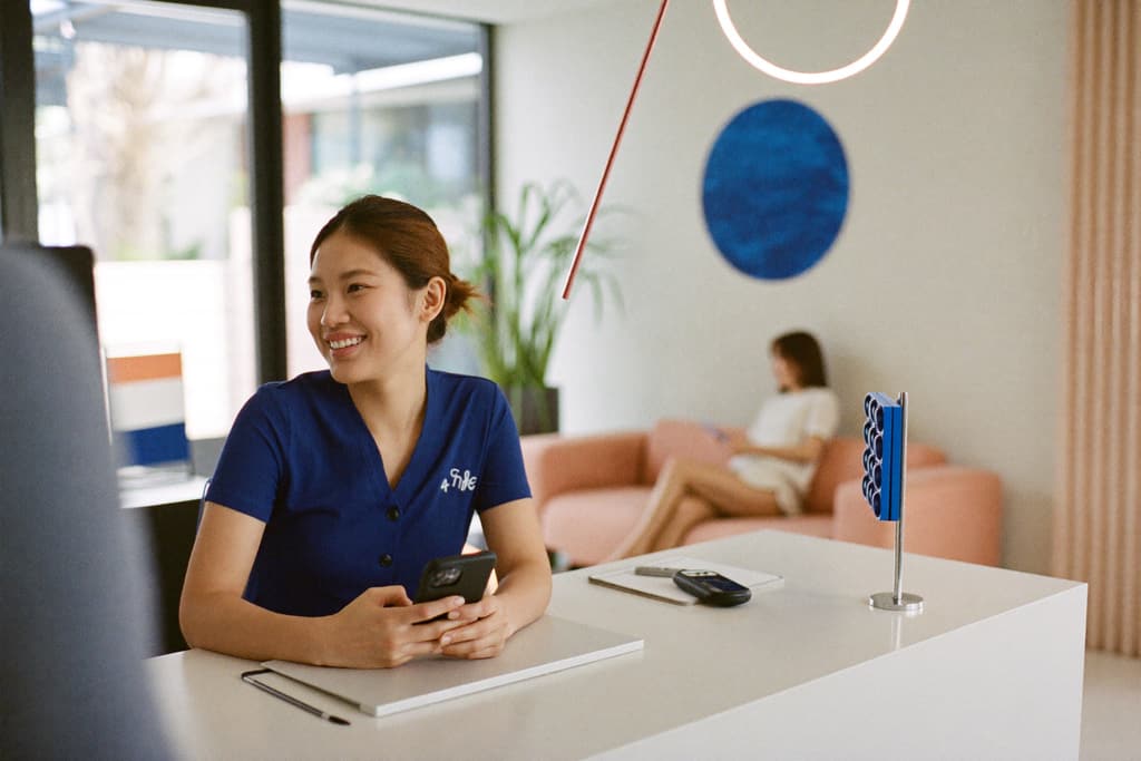 A receptionist at a med spa front desk smiles while holding her phone.